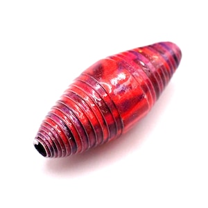 May include: A red and purple paper bead with a glossy finish. The bead is oval-shaped and has a spiral design. The bead is a craft supply for jewelry making or other creative projects.