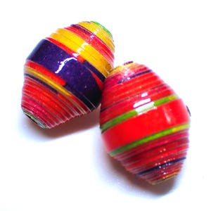 May include: Two colorful, handmade paper beads. One bead features layers of red, purple, yellow, and green. The other bead is primarily red with green and purple stripes. These beads are ideal for jewelry making.