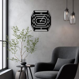May include: A black geometric wall clock with a unique hexagonal design. The clock features the numbers 12 and 6, and the hands are visible. The clock is mounted on a gray wall in a modern living room setting.