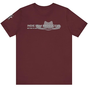 May include: A maroon t-shirt featuring the text "INIE FILM PRODUCERS" above a fedora graphic. Below the graphic is the text "BETTER TO ASK FORGIVENESS THAN PERMISSION." A small graphic is on the left sleeve.