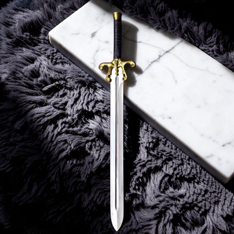 May include: A decorative sword with a silver blade and a gold-colored hilt. The handle is wrapped in black material. The sword is displayed on a white marble surface and a dark gray, fluffy rug.