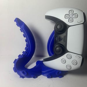 Könnte beinhalten: Ein blauer, oktopusförmiger Controller-Ständer, der einen weiß-schwarzen Gamecontroller hält. Der Ständer ist 3D-gedruckt und weist detaillierte Tentakeldesigns auf. Der Controller hat Knöpfe und Joysticks.