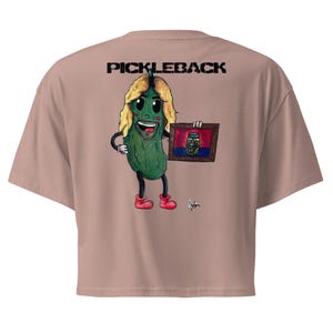 May include: A dusty rose crop top featuring a cartoon pickle character holding a framed picture of a pickle jar. The pickle has blonde hair, red shoes, and the word "PICKLEBACK" is printed across the top.