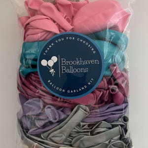 May include: A clear plastic bag filled with a balloon garland kit. The kit includes balloons in shades of pink, teal, purple, and silver. A circular label reads "Thank you for choosing Brookhaven Balloons Balloon Garland Kit."