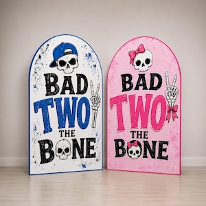 Peut inclure: Deux panneaux décoratifs en forme de pierre tombale. L'un est blanc avec des accents bleus et le texte "BAD TWO THE BONE". L'autre est rose avec le même texte. Chacun présente une tête de mort et des os croisés.