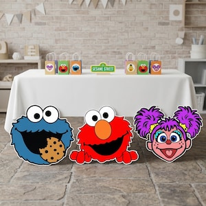 May include: Colorful Sesame Street-themed party decorations. Includes cutouts of Cookie Monster, Elmo, and Abby Cadabby. Also features gift bags with character designs and a "Sesame Street" sign. Perfect for a children's birthday party.