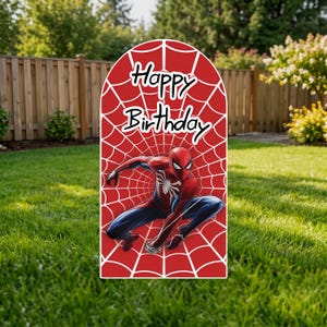 May include: An arched sign featuring a red background with a white spiderweb pattern. The text "Happy Birthday" is printed in black at the top. A graphic of a red and blue costumed character in a crouching pose is centered on the sign.