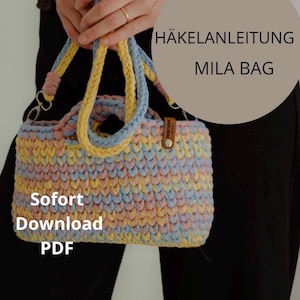 Könnte beinhalten: Eine rechteckige Häkeltasche mit einem mehrfarbigen Muster aus pastellgelbem, hellblauem und zartrosa Garn. Die Tasche hat zwei geflochtene Henkel und ein kleines braunes Lederimitat-Etikett. Der Text lautet HÄKELANLEITUNG MILA BAG und Sofort Download PDF.