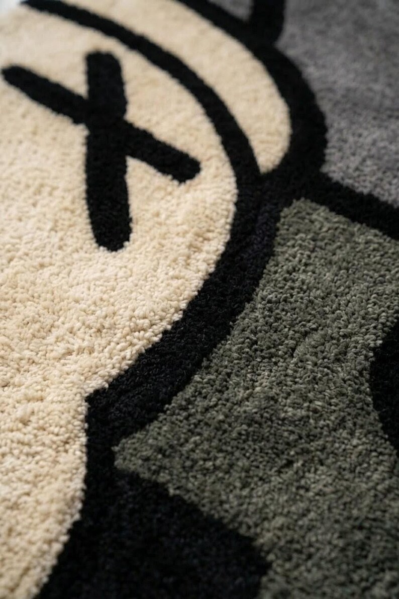 May include: Close-up of a plush rug featuring a graphic design with a repeating pattern. The design incorporates black, off-white, and gray colors. The rug has a soft, textured surface.