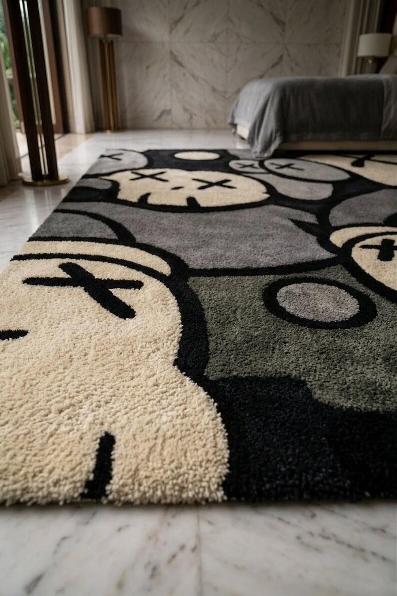 May include: A large, plush area rug with a repeating pattern of stylized cartoon faces in cream, black, and gray. The rug has a soft, textured surface and is placed on a marble floor. The design is modern and playful, suitable for a bedroom or living space.