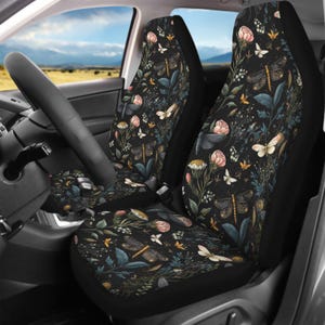 May include: A pair of car seat covers featuring a black background with a botanical pattern of pink flowers, green foliage, and various dragonflies and butterflies in shades of white, yellow, and brown, covering the front seats of a vehicle.