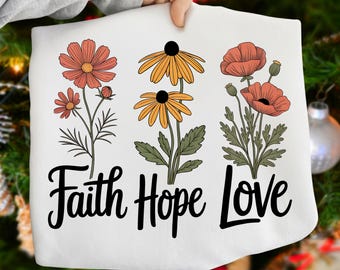 May include: White fabric with a floral design featuring orange, yellow, and red flowers. The words "Faith Hope Love" are written in black script below the flowers. The fabric is held up by a person.