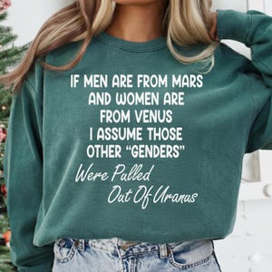 May include: A teal green sweatshirt with white text. The text reads: "IF MEN ARE FROM MARS AND WOMEN ARE FROM VENUS I ASSUME THOSE OTHER 'GENDERS' Were Pulled Out Of Uranus."