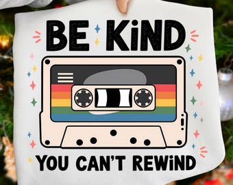 Könnte beinhalten: Weißes Sweatshirt mit einem Retro-Kassettenband-Design. Das Kassettenband hat einen Regenbogenstreifen und die Worte "BE KIND YOU CAN'T REWIND" in schwarzer Schrift. Das Design ist von bunten Sternakzenten umgeben.