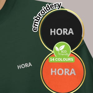 May include: Dark green sweatshirt with the word "HORA" embroidered in white. The image also features a circular design with the text "HORA" in white on a black background and on an orange background. The design includes the text "Eco Friendly" and "14 COLOURS".