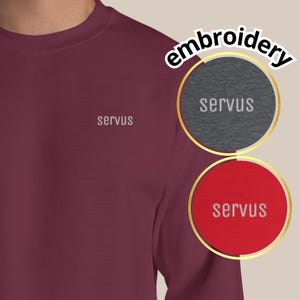May include: A maroon sweatshirt with the word "servus" embroidered in white on the chest. The image also shows two circular examples of the embroidery, one on gray and one on red, with the word "servus" in white.