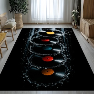 May include: Black rectangular area rug featuring a design of vinyl records with colorful labels, including yellow, red, blue, and orange. Water splashes surround the records, creating a dynamic visual effect. The rug is placed on a light-colored wooden floor.