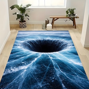 May include: A rectangular area rug featuring a digitally rendered image of a deep, dark hole in a frozen lake. The rug's design showcases shades of blue and white, creating an illusion of depth and texture. The rug is placed on a wooden floor.