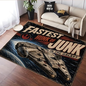 Op de afbeelding: Rechthoekig vloerkleed met een gedetailleerde illustratie van het Millennium Falcon ruimteschip en de tekst "Fastest Hunk of Junk in the Galaxy". Het vloerkleed heeft een verweerde, vintage uitstraling met een donkerblauw en bruin kleurenschema.
