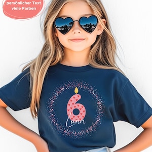 K&ouml;nnte beinhalten: Ein marineblaues T-Shirt mit einer rosa Zahl sechs, verziert mit roten Herzen, einer Kerze und dem Namen "Luna" in wei&szlig;er Schrift. Das Design ist von einem gepunkteten Muster umgeben. Das Bild enth&auml;lt auch herzf&ouml;rmige Sonnenbrillen und Text in einer rosa Blase.