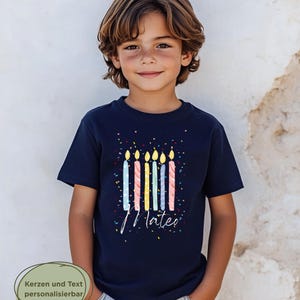 May include: A navy blue t-shirt featuring a colorful birthday candle design with the name "Mateo" in white script. The shirt has a confetti pattern and is worn by a young person.