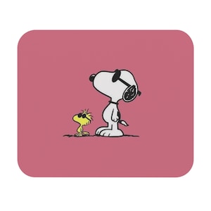 Può includere: Un tappetino per mouse quadrato rosa con un'illustrazione di Snoopy con gli occhiali da sole, in piedi accanto a Woodstock, che indossa anche gli occhiali da sole. I personaggi sono in bianco e nero con accenti gialli.