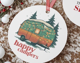 Op de afbeelding: Twee ronde witte kerstversieringen met rode linten. Eén ornament heeft een illustratie van een vintage camper met de rode woorden "happy campers". Het andere ornament heeft "The Smiths 2025" in rode tekst.