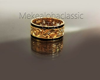 May include: A gold ring with a black band and intricate floral designs. The ring is on a reflective surface.