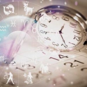 以下が含まれることがあります： 銀色の懐中時計がカレンダーの上に置かれ、背景にはぼやけた黄道十二宮の車輪があります。時計の文字盤には時間が表示されています。黄道十二宮の車輪には、紫と白の背景に白いシンボルがあります。
