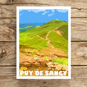 May include: A print featuring a stylized landscape of Puy de Sancy, a mountain in France. The artwork depicts a green hillside with winding paths under a blue sky. The text "PUY DE SANCY" is displayed in white at the bottom of the print.