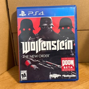 May include: A blue PlayStation 4 game case for Wolfenstein: The New Order. The cover features three silhouetted figures in helmets with glowing red eyes against a red and black background. It includes an M rating and a Doom Beta invite label.