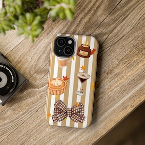 May include: A phone case featuring a pattern of vertical beige and white stripes decorated with illustrations of a pumpkin pie, a candle, a martini glass, a plaid bow, and small orange autumn leaves scattered across the surface.