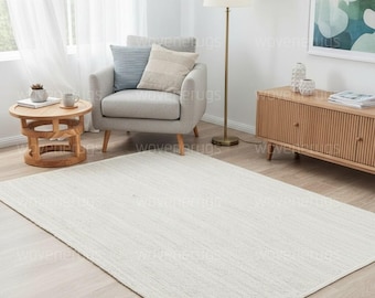 May include: A large, rectangular, off-white rug with a textured surface. The rug is placed on a light-colored wooden floor in a living room setting. The room includes a gray armchair, side table, and a floor lamp.