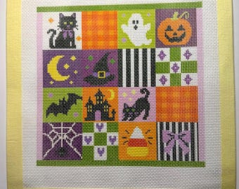 May include: A square needlepoint canvas featuring a grid of twelve Halloween-themed squares. Designs include a black cat, ghost, pumpkin, witch hat, bat, haunted house, spider web, and candy corn, all bordered by a pale yellow fabric tape edge.