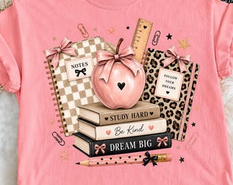 May include: A light pink t-shirt featuring a graphic of a pink apple with a bow, two spiral notebooks with checkered and leopard patterns, three stacked books labeled "STUDY HARD," "Be Kind," and "DREAM BIG," a ruler, and a polka-dot pencil.