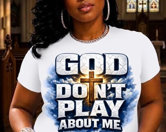 May include: A white short-sleeved t-shirt featuring a graphic print with the text "GOD DO N'T PLAY ABOUT ME" in large, cracked, metallic-style lettering. The design includes a central wooden cross set against a backdrop of blue sky and clouds.