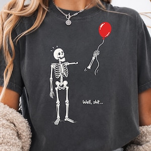 Charcoal Halloween shirt featuring Well Shit funny skeleton design, gothic skeleton artwork and floating red balloon.