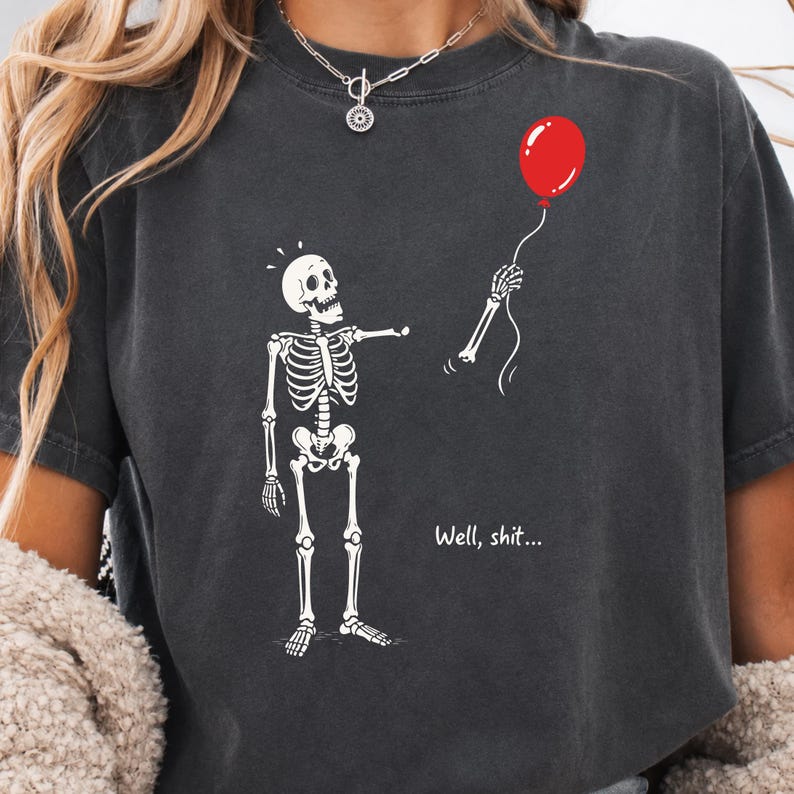 Charcoal Halloween shirt featuring Well Shit funny skeleton design, gothic skeleton artwork and floating red balloon.