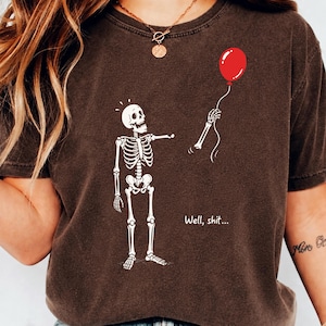 Brown shirt mockup featuring Skeleton Lost Balloon, Well Shit skeleton quote and funny gothic Halloween shirt design.