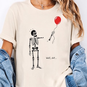 Cream shirt mockup with Well Shit funny skeleton, red balloon and dark humor Halloween PNG SVG design.