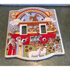 May include: A decorative light switch cover featuring a colorful illustration of Noah's Ark. The design includes a rainbow, sun, moon, and various animals. The cover has two switch openings and is made of ceramic.