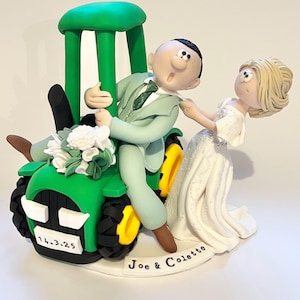 Könnte beinhalten: Ein skurriler Tortenaufsatz für eine Hochzeit mit einem grünen Traktor, einem Bräutigam im Anzug und einer Braut im weißen Kleid. Der Traktor hat gelbe Räder und einen Strauß weißer Blumen. Auf der Basis steht "Joe & Colette" und das Datum "14.3.25".