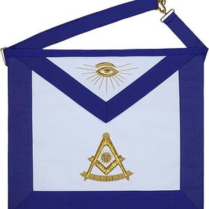 May include: A white apron with a blue border and strap, featuring gold embroidery. The embroidery includes an eye with sun rays and a compass and square symbol. The apron is designed with a v-shaped top and a rectangular bottom.