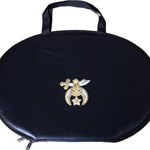 May include: A black, oval-shaped carrying case with a top handle and a zipper closure. The case features a decorative gold emblem with red and white accents. The emblem includes a crescent moon, star, and sword design.