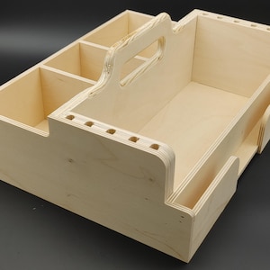 May include: A light-colored wooden organizer with multiple compartments and a handle. The organizer has a large central space, several smaller sections, and side pockets. It is designed for storage and organization.
