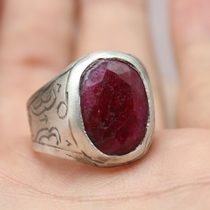 May include: A silver ring with an oval, deep red gemstone. The ring has decorative etchings on the band and is set against a neutral background. The jewelry is from Classi Fine Jewelry.