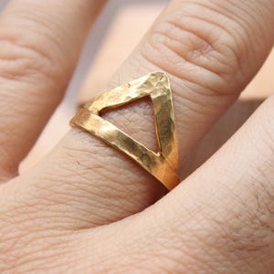 Peut inclure: Une bague dorée avec une texture martelée et un design triangulaire. La bague est portée au doigt. L'image comprend également le logo "Classi finejewelry" dans un carré noir.