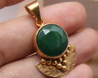 May include: A gold pendant featuring a large, round, faceted green gemstone. The pendant has a textured gold base with small, round details. The pendant is held in a hand.