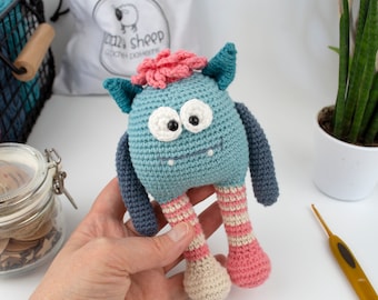 May include: A crocheted blue monster toy with pink and white striped legs, white eyes, and a pink flower on its head.