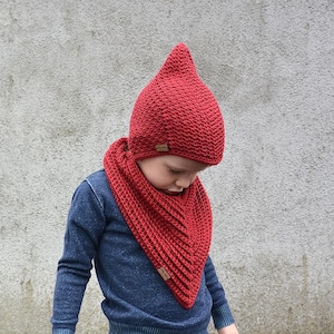 Op de afbeelding: Een kind draagt ​​een rode gebreide muts met een puntige top en een bijpassende rode gebreide sjaal. De muts en sjaal zijn beide gehaakt.